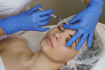 Aesthetic cosmetology. Facelift in spa salon. Beautician makes injections girl in eyebrows....