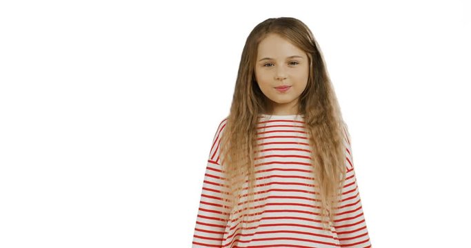 Funny small schoolgirl with long hair standing on the chroma key background, showing her tangue to the camera and crossing her hands. White wall on the back.