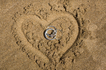 Fototapeta na wymiar Wedding rings in heart sand