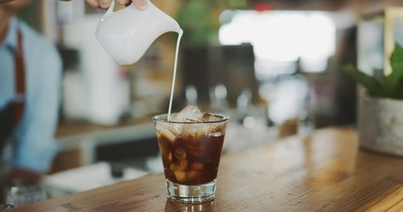 Attractive female barista pouring milk into coffee, close up of hand pouring milk, artisan coffee shop lifestyle