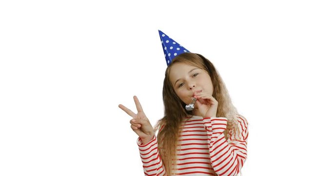 Caucasian cute small teen girl with a long hair in the birthday party hat blowing in the horn and doing victory gesture. White screen background.