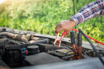 Close up hand of car technician holding cable to connect to battery, Car mechanic uses battery jumper cables charge a dead battery, A car mechanic uses battery jumper cables transferring power.