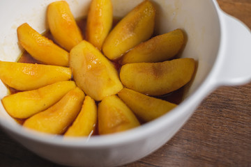 Cooked apple pieces with caramel arrange in a white bowl on wood table top.