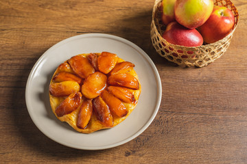 Apple Tarte Tatin on a plate with red apple in basket as props.