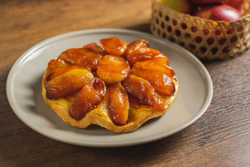 Apple Tarte Tatin on a plate with red apple in basket as props.