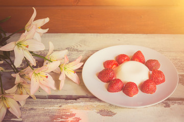 Lily flowers and homemade italian dessert panna cotta with strawberry on aged wooden table.