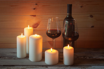 Fototapeta na wymiar Bottle of red wine, glasses of red wine and candles on aged wooden table.