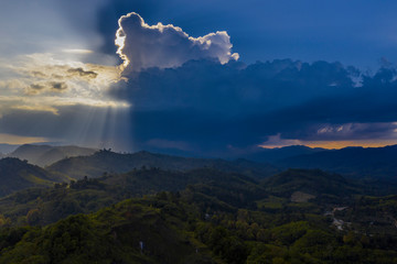 Epic cloudy sunset in green hills landscape , sun rays shining through heavy rainy clouds