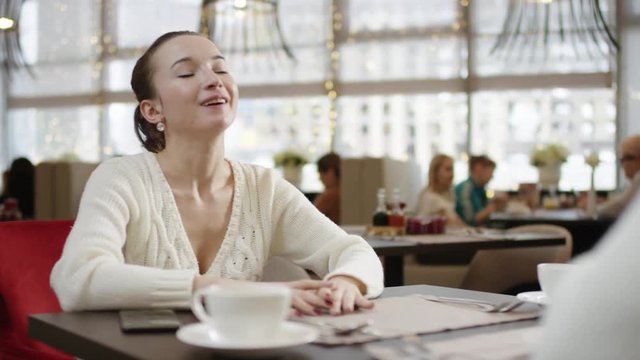Young woman laughing while chatting with her friend in a restaurant