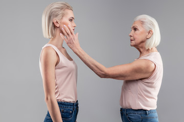 Serious tidy senior lady petting her short-haired young version