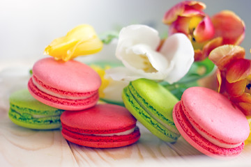 French macarones red, pink and green on a wooden background next to spring flowers. Sweet dessert from France, colorful cookies made from almond flour and egg whites.Confectionery background