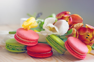 French macarones red, pink and green on a wooden background next to spring flowers. Sweet dessert from France, colorful cookies made from almond flour and egg whites.Confectionery background