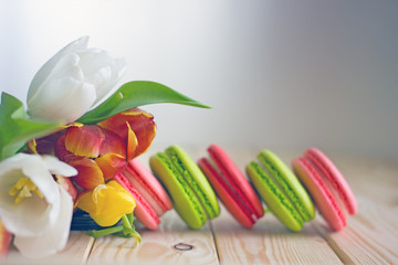 French macarones red, pink and green on a wooden background next to spring flowers. Sweet dessert from France, colorful cookies made from almond flour and egg whites.Confectionery background