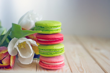 French macarones red, pink and green on a wooden background next to spring flowers. Sweet dessert from France, colorful cookies made from almond flour and egg whites.Confectionery background