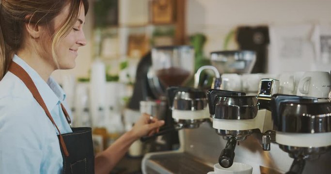 Smiling attractive female barista working in coffee shop, barista preparing espresso, artisan coffee shop lifestyle