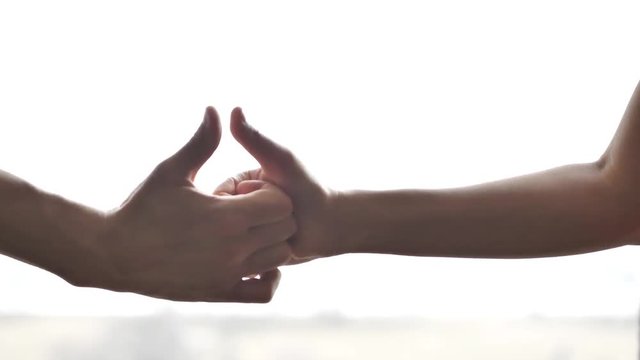 Close up of a man and woman hands and arms having a thumb war with their fingers in front of a window with lots of bright white sunlight coming through the glass.