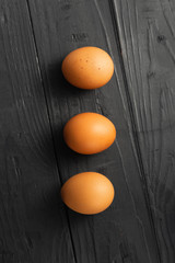 Three chicken eggs dark wooden background top view