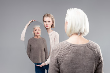 Serious blonde girl showing her mother with help of oval mirror