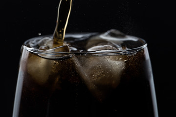 Glass of pouring fizzy drink with ice on a black background