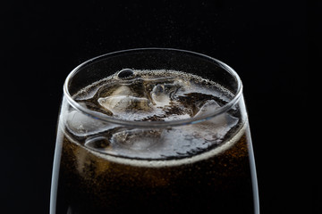 A glass of cola beverage with a salt. On a black background.