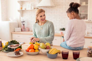 Loving blonde mother cutting fruits for her lovely cut daughter