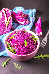 Healthy salad with red cabbage and arugula in purple bowl on a dark background. Vegetarian concept