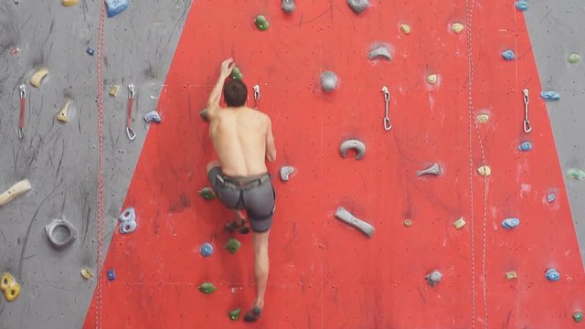 Strong man enjoying rock climbing in sport center. Athlete trying to reach the goal, slow motion