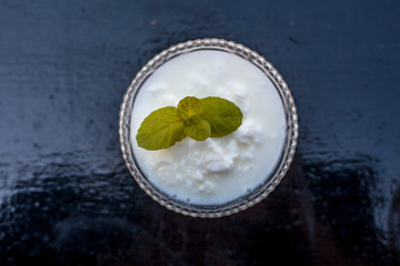 Close up of raw organic curd in a glass bowl along with mint leaf on the top for decoration on wooden surface.