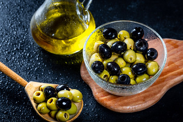 Olive oil in vintage glass bottles with black, green olives and wooden spoon on black background. Copyspace. Flatley. Food background with water drops.Healthy eating and diet concept