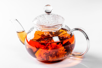 Tea in a glass teapot with a blooming large flower. Teapot with exotic green tea on white background