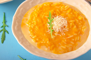 Delicious pumpkin risotto with parmesan cheese in white plate on light blue background