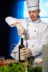 Chef in white uniform opens a bottle of wine