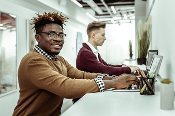 Beaming African American guy in clear glasses working on laptop