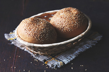 dark and moody stil life photo of sesame buns in a bread basket standing on a napkin on a dark...