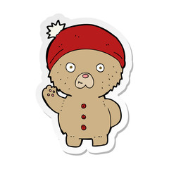 sticker of a cartoon waving teddy bear in winter hat