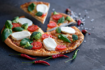Sliced pizza with Mozzarella cheese, tomatoes, broccoli, Spices and fresh basil. Italian pizza. Pizza on black stone background