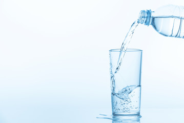 Pouring water from bottle into glass on blue background. Photo with copy space.