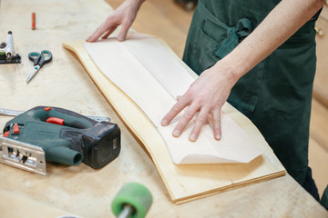 Hands of the master carpenter pressed against the board mold to cut a skateboard from a wooden board. Concept of creating exclusive wooden products on order