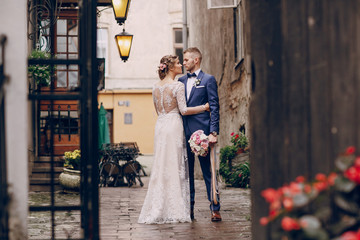 beautiful and elegant blonde bride in a long white dress with her handsome bride in a blue suit wallkig in a raining city