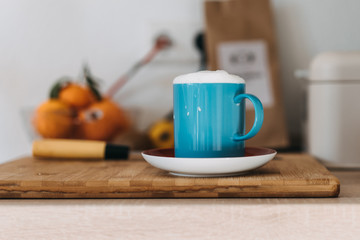 blue coffee cup with milk on a table with oranges in background
