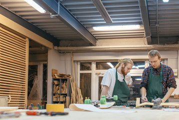Two male carpenters a teacher and a student are working on a new product in their carpentry workshop. Concept of creating a new wooden handmade goods