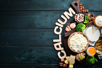 Products containing natural calcium: cheese, milk, parmesan, sour cream, fish, almonds, parsley, garlic, broccoli. On a black wooden background. Top view. Free copy space.