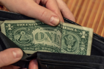 One dollar is lying in an empty leather wallet. No money in the purse. Poverty and unemployment. Old wooden rustic background.
