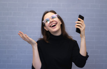 Happy young smiling woman is holding the phone in his hands and is looking away
