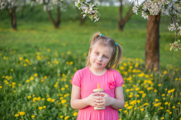 Positive smiling cute blondie girl laughing and drinking milk outdoors in green garden in blossom