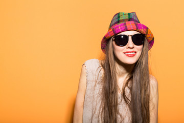 Happy young beautiful woman wearing sunglasses and hat over bright orange background