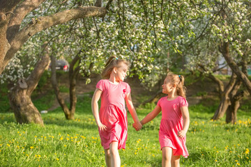 Outdoor portrait of two cheerful pretty girls playing in summer green garden in blossom. Childhood, summer, children games concept