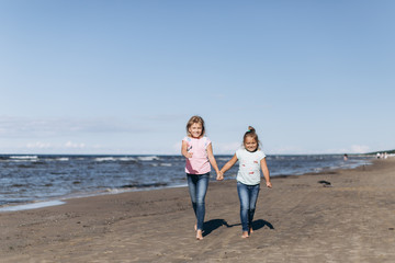 Cheerful happy girls running on the coast of the ocean with wind and waves. Happiness, activity, ocean, childhood concept