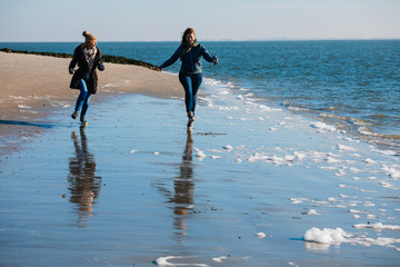 Two friends run along the seashore. Women Friendship. Beach. North Sea. Sunny weather. Coldly.