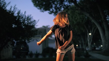 Happy 8 year old girl dancing the floss dance moves outdoors on suburban street at dusk. Slow motion, 4K UHD.